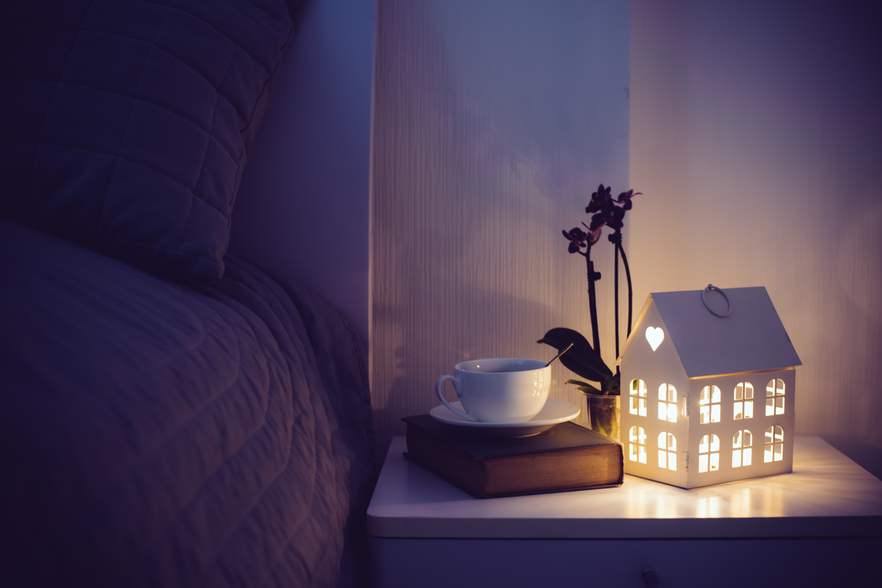 Cozy evening bedroom interior, cup of tea and a night light on the bedside table. Home interior decor with warm light.